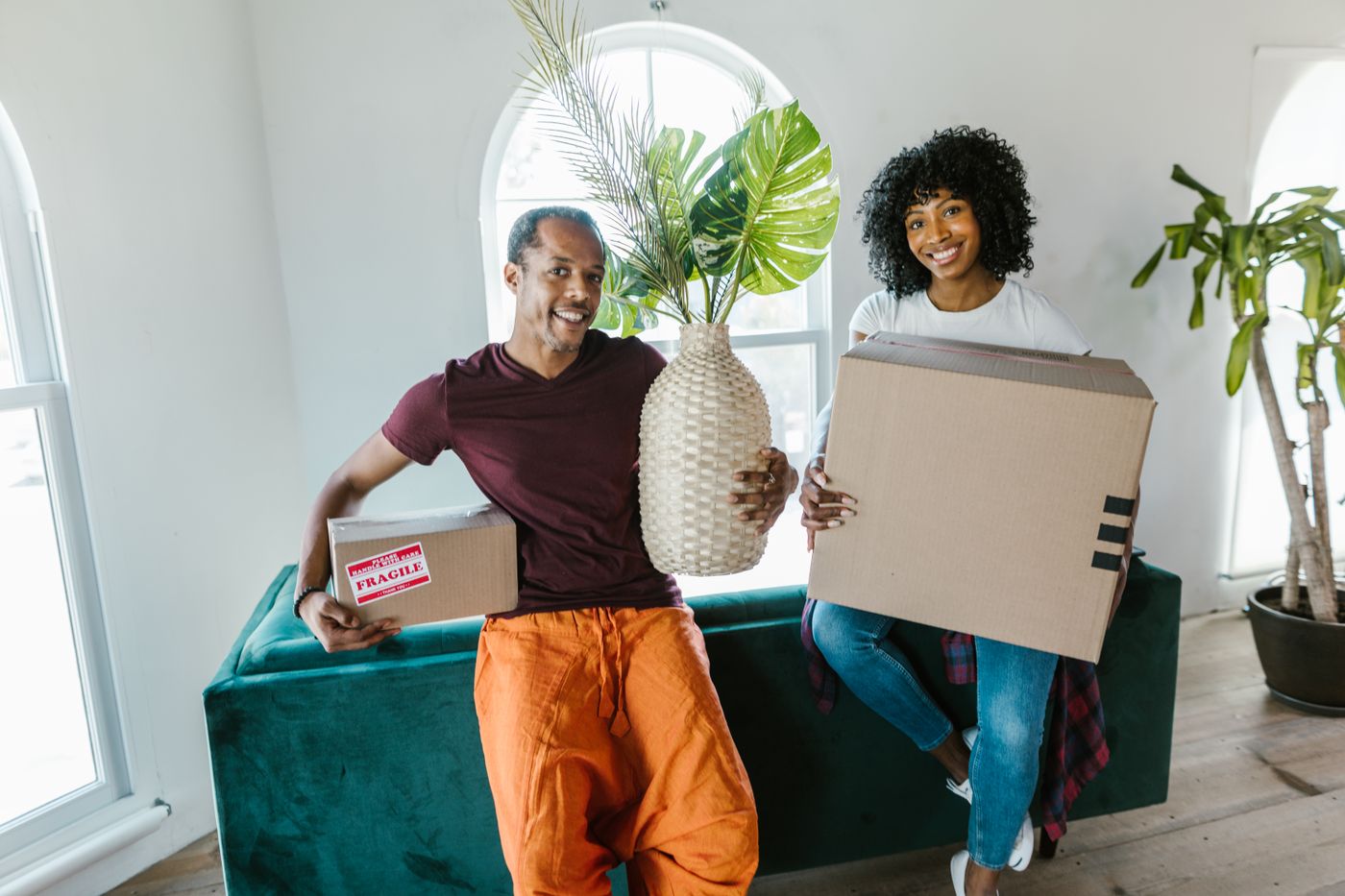 Couple carrying moving boxes and a plant into their new home, illustrating furniture removals in Roodepoort